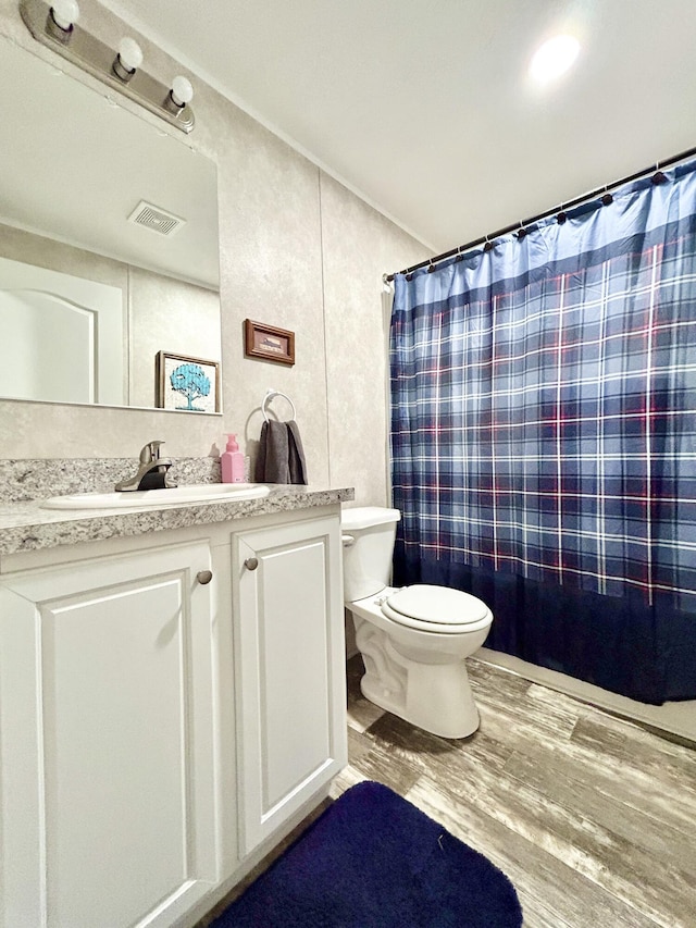 bathroom with vanity, toilet, wood finished floors, a shower with curtain, and visible vents