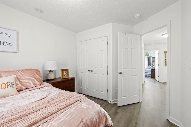 bedroom featuring a closet, baseboards, a textured ceiling, and wood finished floors