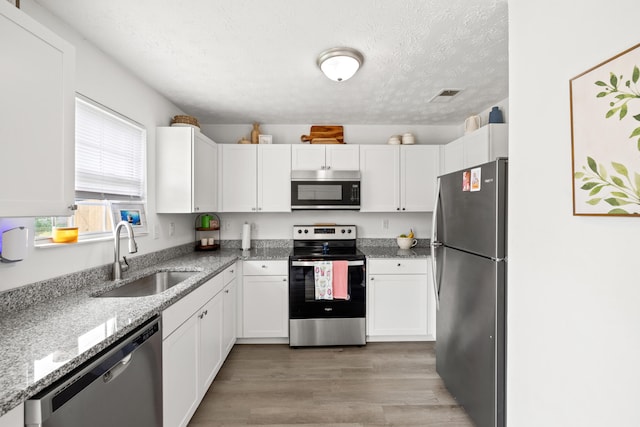 kitchen with visible vents, a textured ceiling, white cabinetry, a sink, and stainless steel appliances
