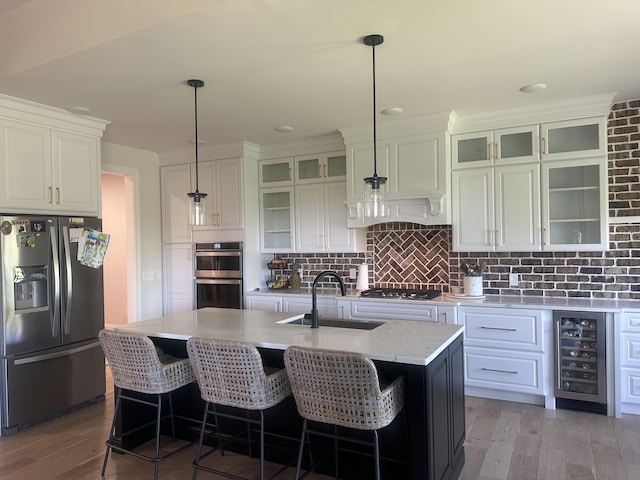 kitchen featuring backsplash, appliances with stainless steel finishes, a sink, light wood finished floors, and beverage cooler