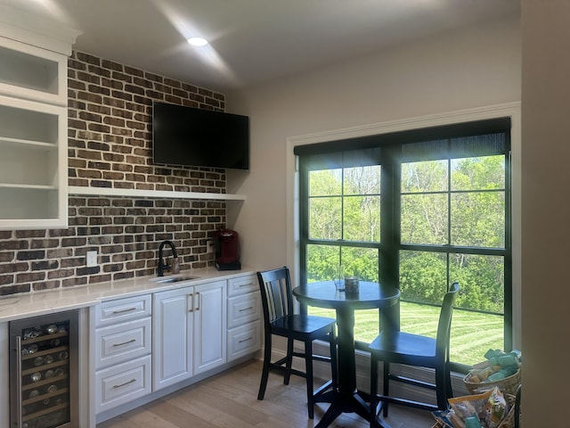 bar with beverage cooler, decorative backsplash, a sink, and light wood-type flooring