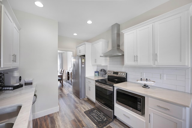 kitchen featuring wall chimney range hood, appliances with stainless steel finishes, white cabinetry, wood finished floors, and backsplash