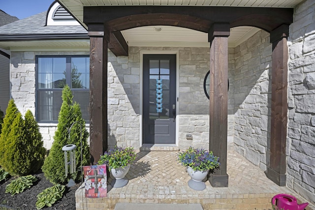 view of exterior entry featuring a shingled roof and stone siding