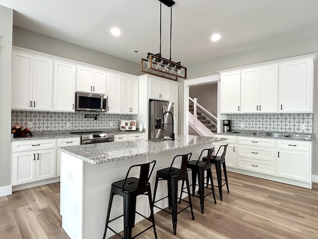 108 Patriot Dr, Science Hill, KY 42553 - kitchen featuring stainless steel appliances, decorative backsplash, light wood finished floors, a breakfast bar, and white cabinets