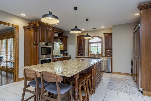 kitchen with a sink, stainless steel appliances, baseboards, light tile patterned floors, and a center island with sink