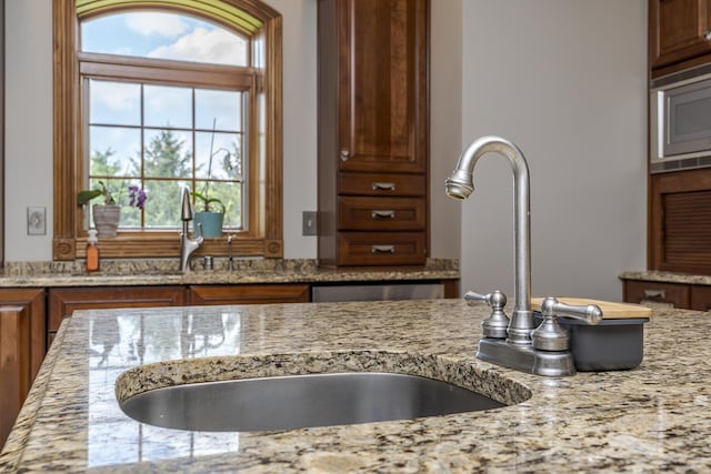 details featuring a sink, stainless steel microwave, brown cabinets, and light stone countertops
