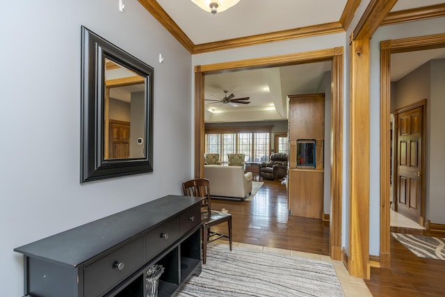 hallway with crown molding, a raised ceiling, baseboards, and wood finished floors