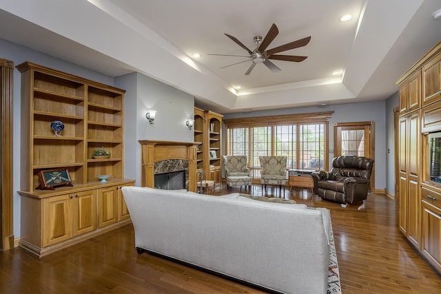 living area featuring ceiling fan, a fireplace, a raised ceiling, recessed lighting, and dark wood-type flooring