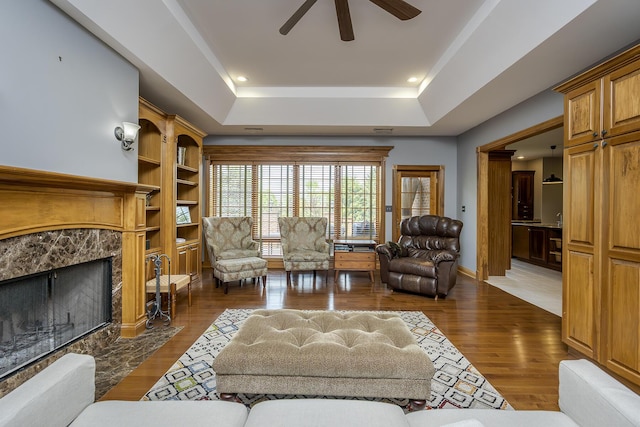 living room with a ceiling fan, a high end fireplace, dark wood finished floors, a raised ceiling, and recessed lighting