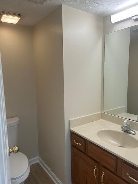 bathroom with toilet, a textured ceiling, wood finished floors, and vanity
