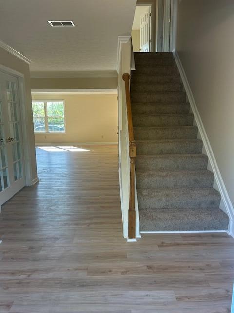 staircase with crown molding, baseboards, wood finished floors, and visible vents