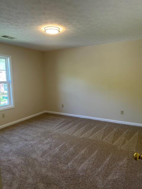 unfurnished room with visible vents, a textured ceiling, baseboards, and dark colored carpet