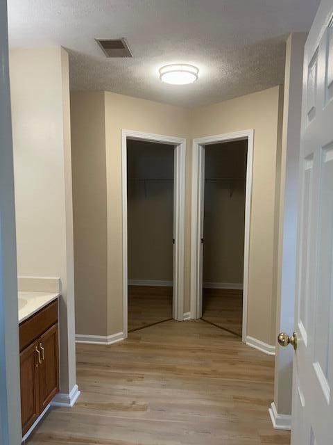 corridor with a textured ceiling, visible vents, baseboards, and light wood-type flooring