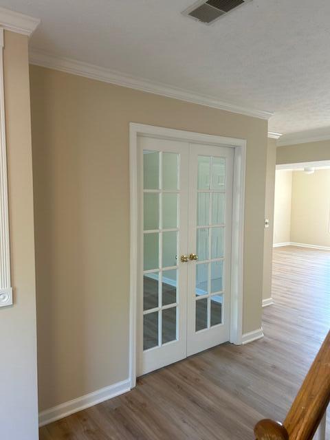 entryway with french doors, visible vents, wood finished floors, baseboards, and ornamental molding
