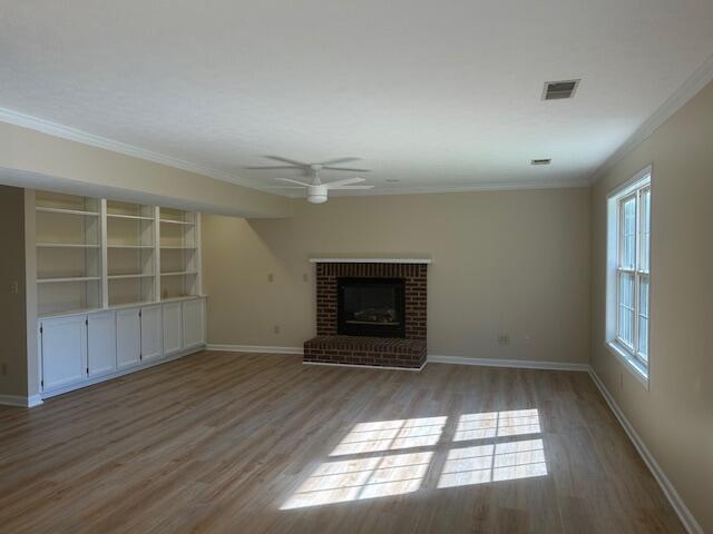 unfurnished living room with ceiling fan, visible vents, ornamental molding, and wood finished floors