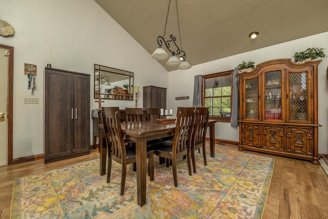 dining room featuring high vaulted ceiling, light wood-style flooring, and baseboards