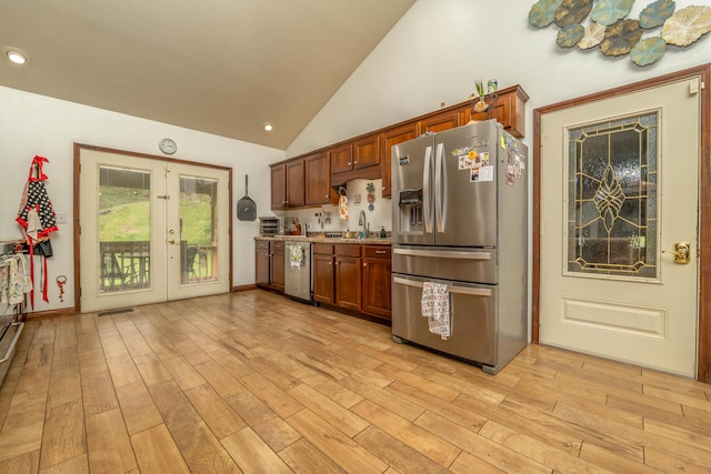 kitchen with stainless steel appliances, french doors, lofted ceiling, light wood finished floors, and brown cabinetry
