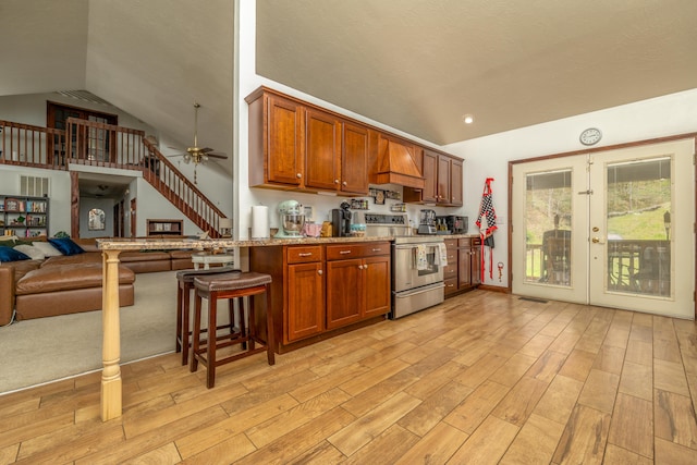 kitchen featuring stainless steel electric range oven, custom range hood, light wood-style floors, french doors, and lofted ceiling