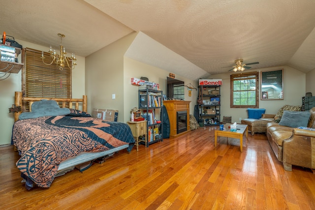 bedroom featuring a chandelier, wood finished floors, lofted ceiling, a glass covered fireplace, and a textured ceiling