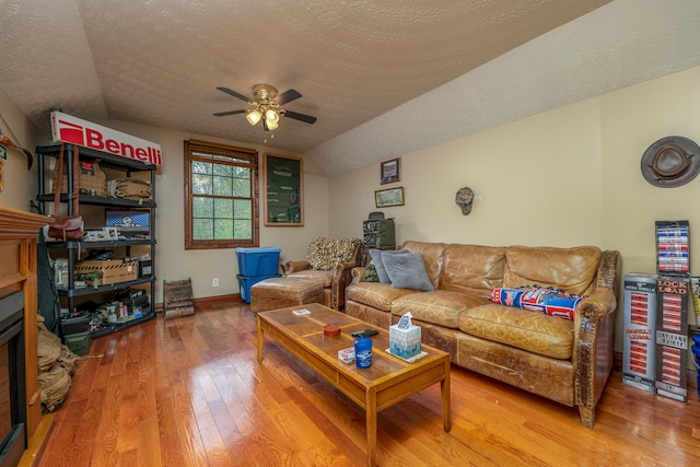 living area with wood finished floors, ceiling fan, vaulted ceiling, a textured ceiling, and a fireplace