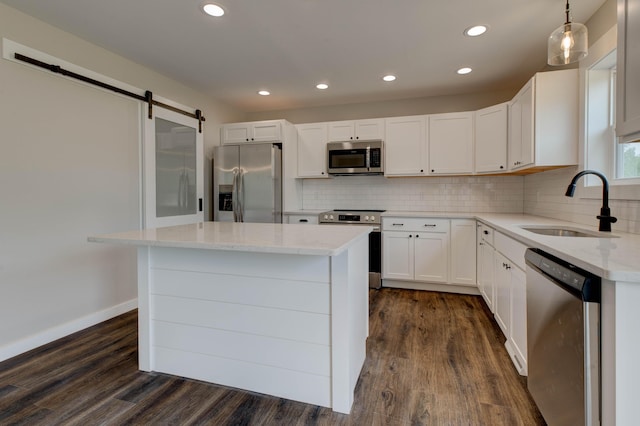 kitchen with dark wood-style flooring, appliances with stainless steel finishes, a barn door, a sink, and light stone counters