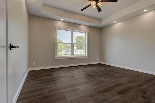 unfurnished room featuring a ceiling fan, a tray ceiling, dark wood finished floors, and baseboards