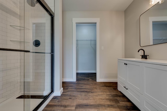 bathroom featuring a walk in closet, a stall shower, wood finished floors, vanity, and baseboards