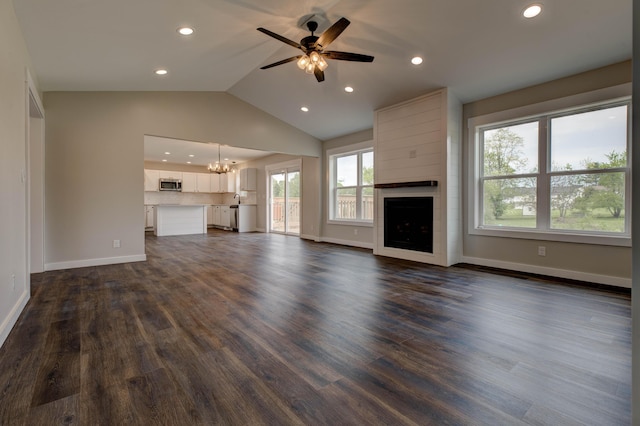 unfurnished living room with a large fireplace, vaulted ceiling, ceiling fan with notable chandelier, recessed lighting, and dark wood-type flooring
