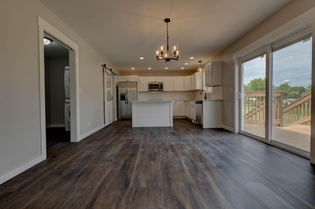 kitchen with stacked washer / drying machine, a notable chandelier, appliances with stainless steel finishes, a barn door, and dark wood-style floors