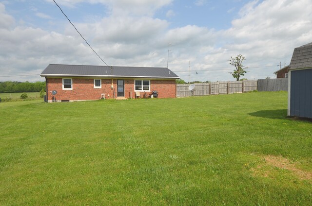 back of property featuring brick siding, fence, a yard, and metal roof