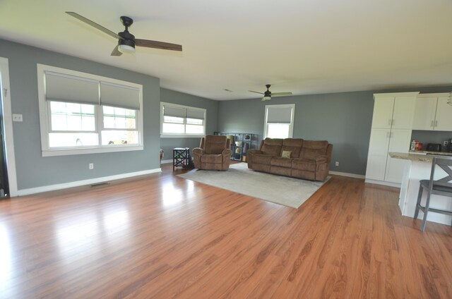 living area with baseboards, a ceiling fan, light wood finished floors, and visible vents