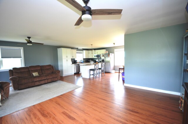 living area with baseboards, a ceiling fan, and wood finished floors