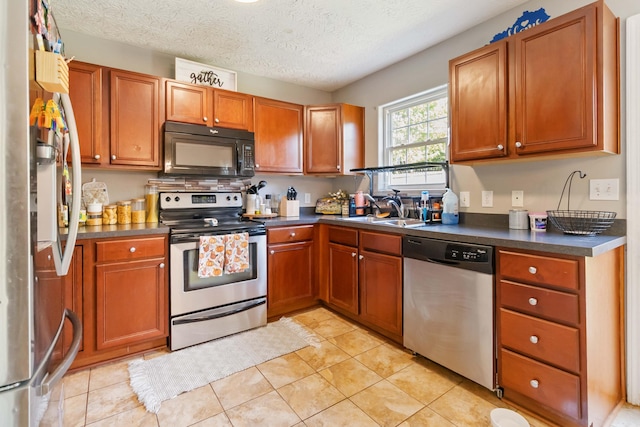 kitchen with brown cabinetry, dark countertops, a sink, light tile patterned floors, and stainless steel appliances
