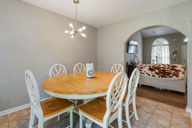 dining room with an inviting chandelier, arched walkways, light tile patterned floors, and baseboards