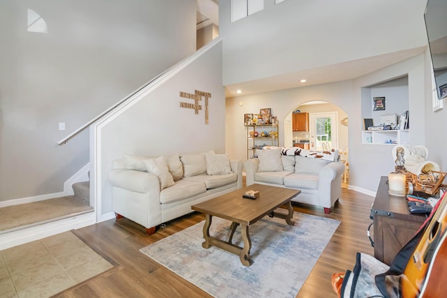 living room featuring arched walkways, stairs, wood finished floors, baseboards, and recessed lighting