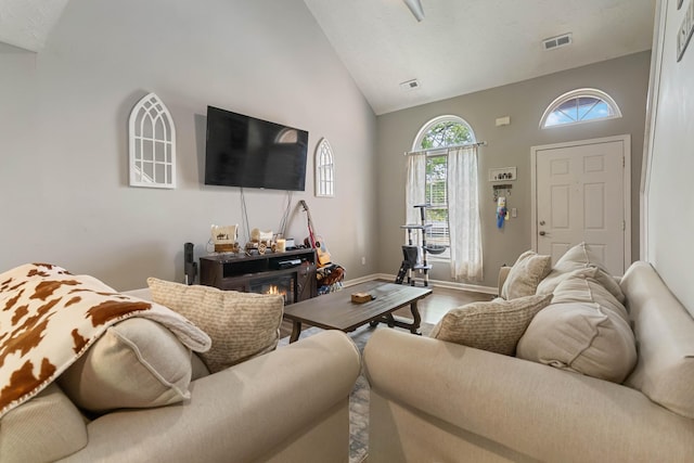 living area featuring visible vents, baseboards, wood finished floors, and high vaulted ceiling