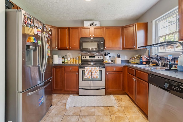 kitchen with brown cabinets, dark countertops, appliances with stainless steel finishes, a sink, and light tile patterned floors