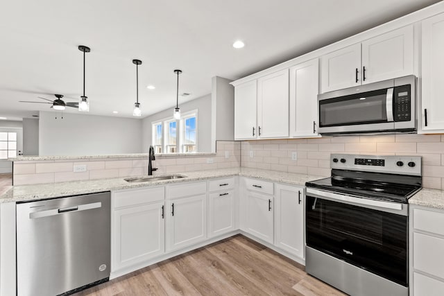 kitchen featuring ceiling fan, appliances with stainless steel finishes, a sink, light wood finished floors, and backsplash