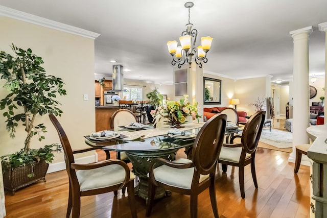 dining area with crown molding, a chandelier, light wood-type flooring, and decorative columns