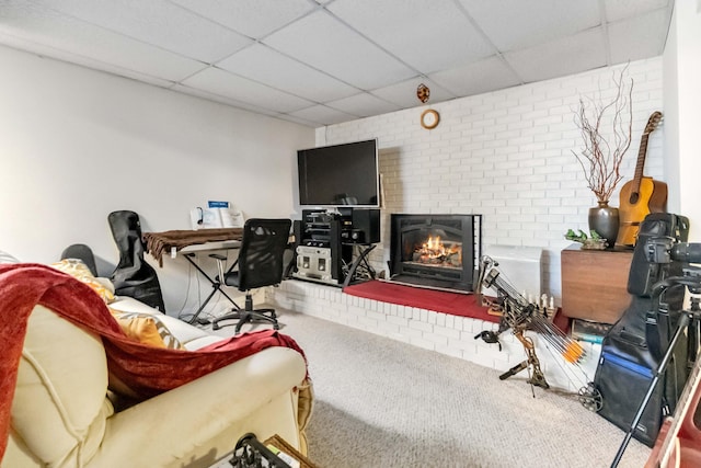 living area featuring a paneled ceiling, a brick fireplace, brick wall, and carpet