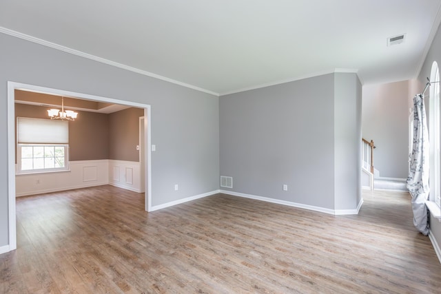 spare room with crown molding, visible vents, an inviting chandelier, and wood finished floors