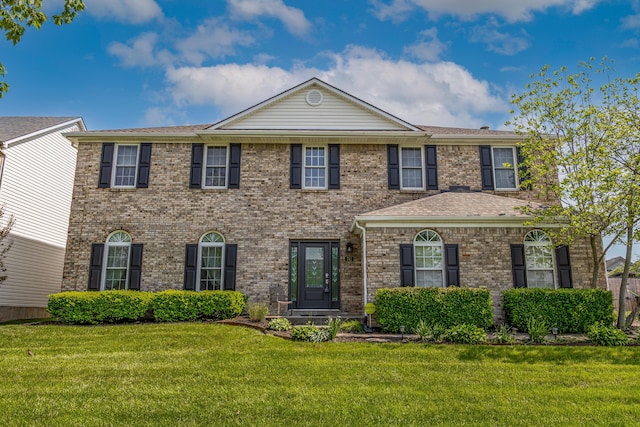 colonial inspired home featuring brick siding and a front yard
