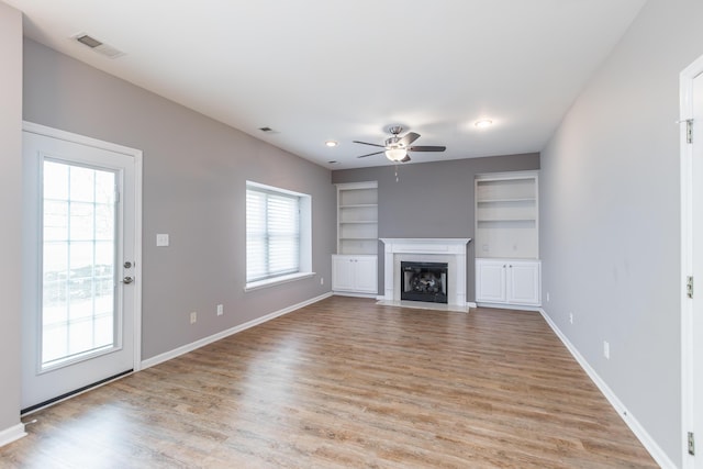 unfurnished living room with a ceiling fan, light wood finished floors, built in shelves, and visible vents