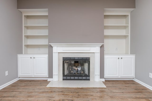 unfurnished living room with built in features, baseboards, a fireplace with raised hearth, and wood finished floors