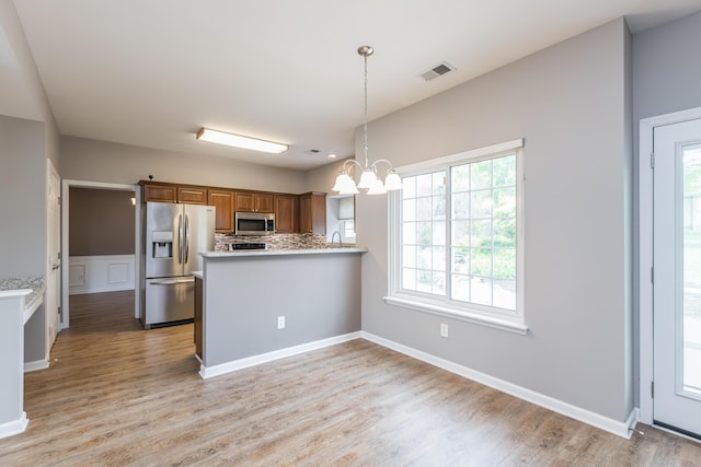 kitchen with visible vents, brown cabinetry, an inviting chandelier, light wood-style flooring, and stainless steel appliances