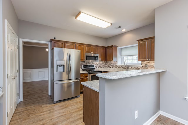 kitchen featuring visible vents, decorative backsplash, a peninsula, light wood-style flooring, and stainless steel appliances