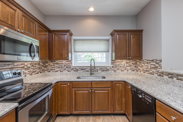 kitchen featuring light stone counters, appliances with stainless steel finishes, a sink, light wood-style floors, and backsplash
