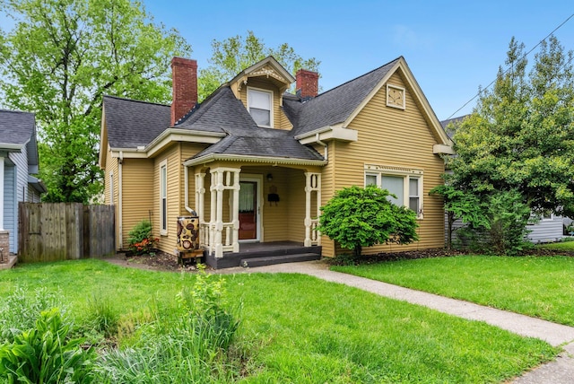 view of front facade with roof with shingles, fence, a porch, a front yard, and a chimney