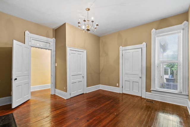 empty room featuring wood-type flooring, baseboards, a notable chandelier, and visible vents