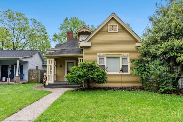 bungalow-style home featuring fence, a shingled roof, a front yard, a chimney, and covered porch